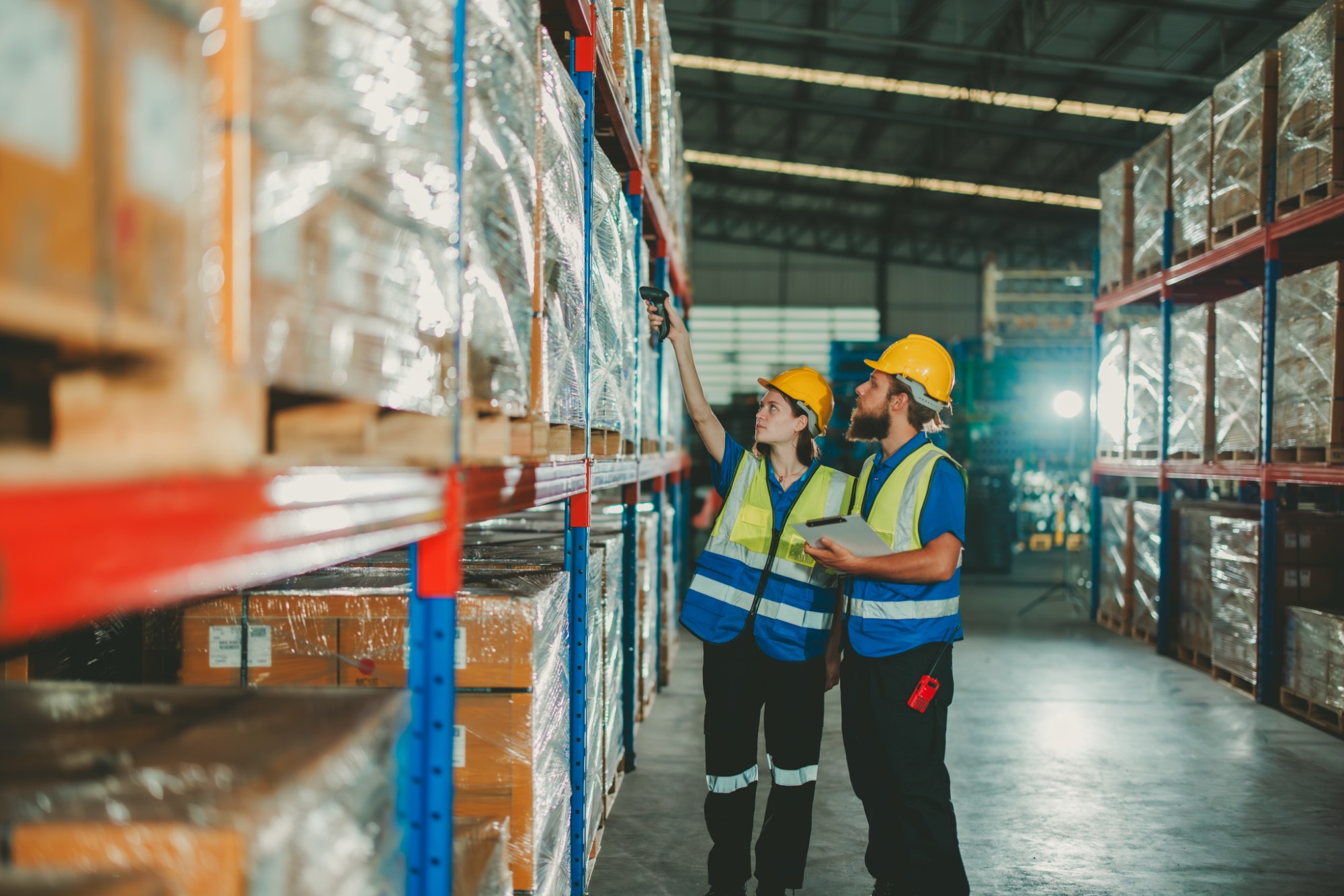 Dos operarios con casco y chaleco escaneando mercadería en las estanterías del depósito